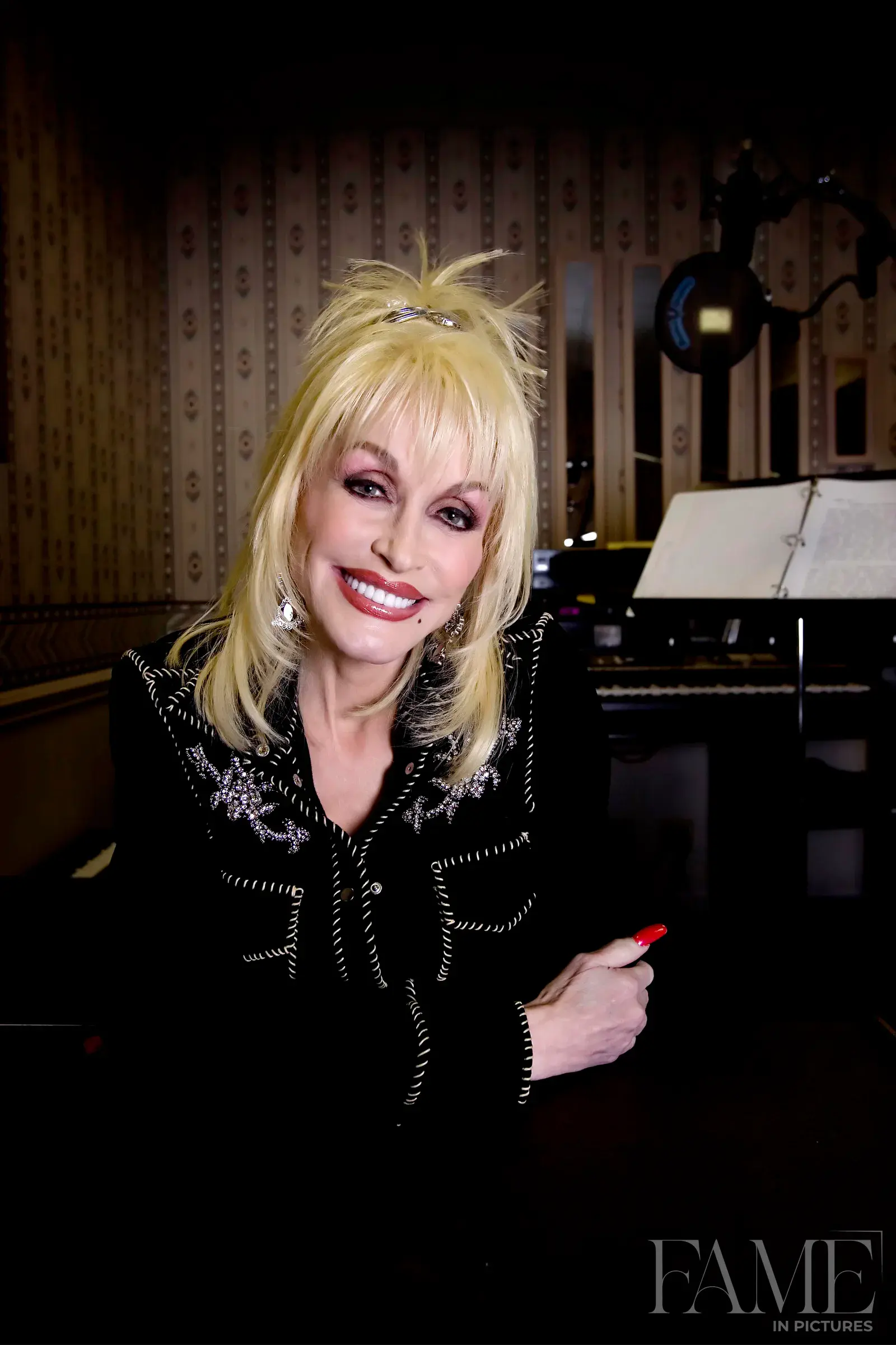 Dolly Parton smiling beside a piano in her Nashville office.