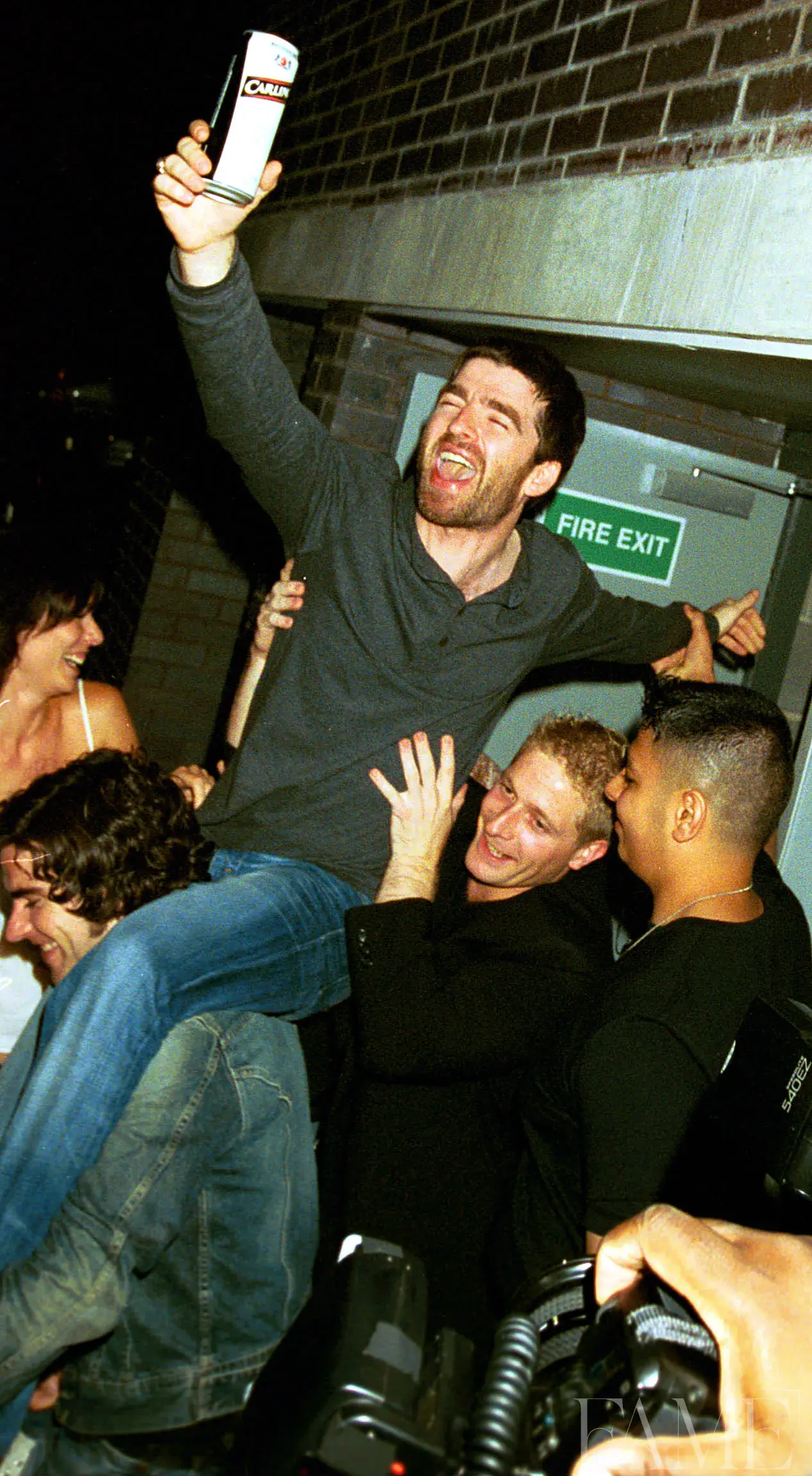 Noel Gallagher holding up a mobile phone in a crowd at the Marquee Club launch in 2002