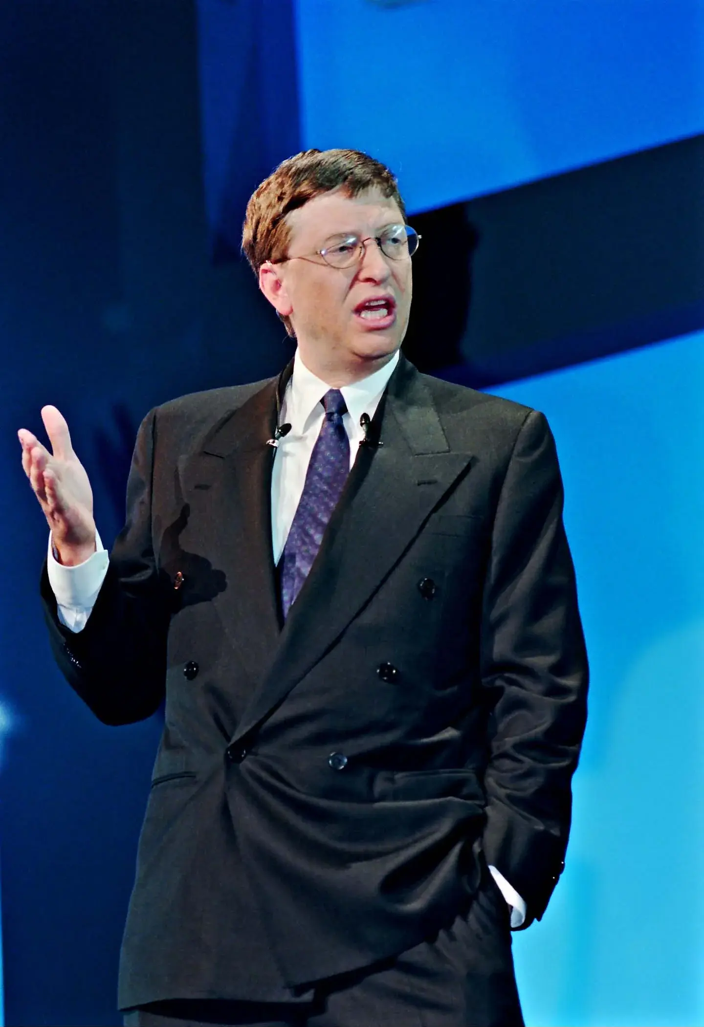 Bill Gates speaking with a raised hand at a Paris internet seminar in 1998