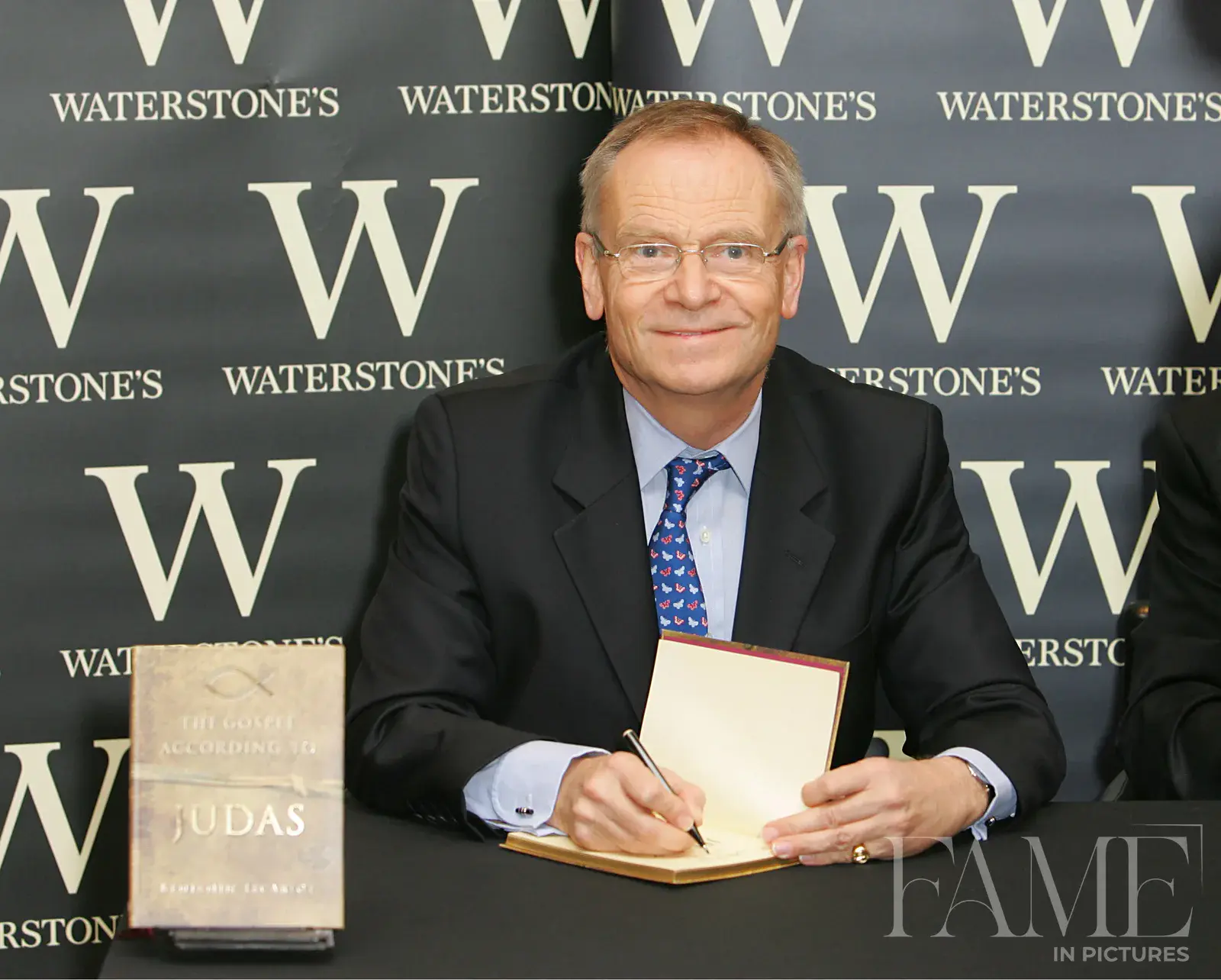 Jeffrey Archer seated at a Waterstones table signing a copy of The Gospel According to Judas