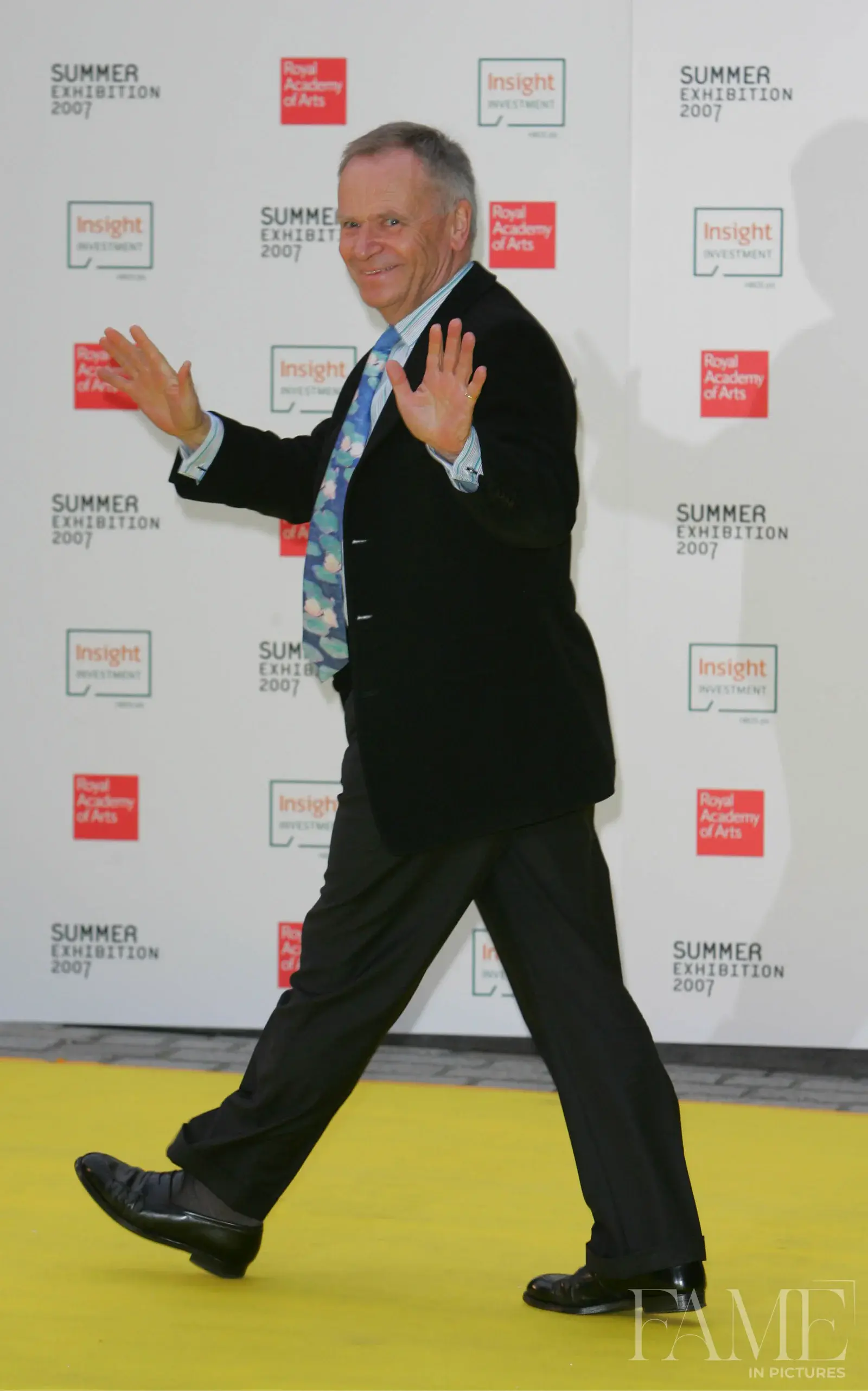 Jeffrey Archer raising his hands before the Royal Academy Summer Exhibition backdrop