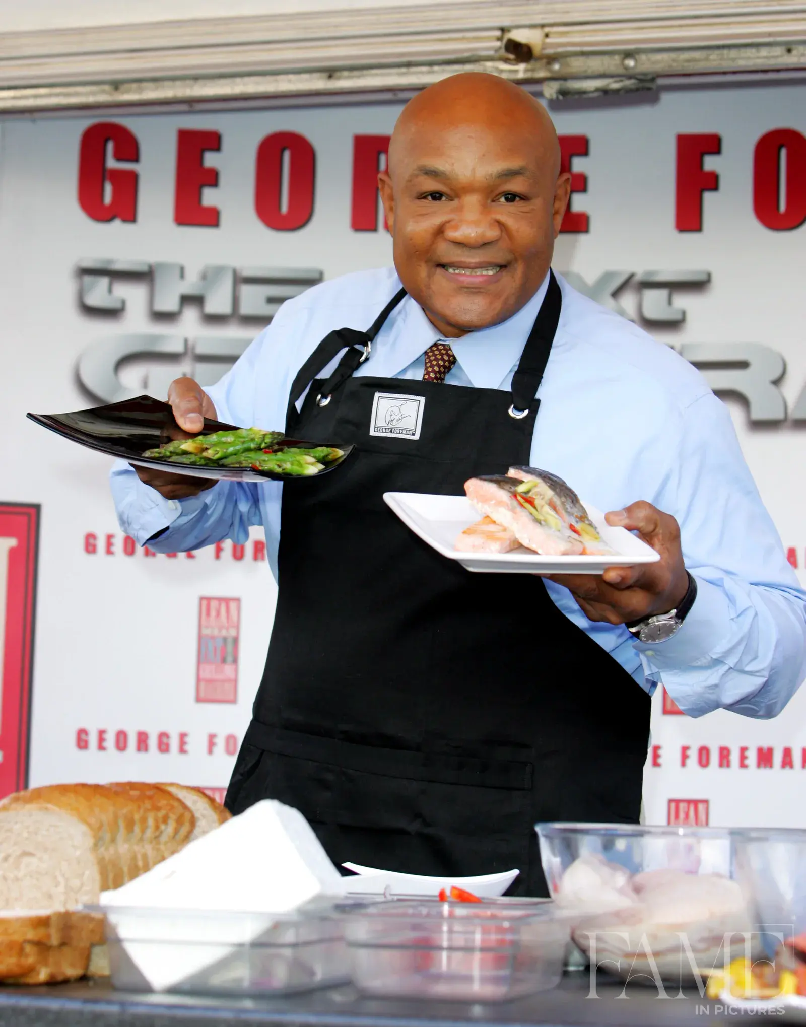 George Foreman smiling towards the camera while holding two plates of food