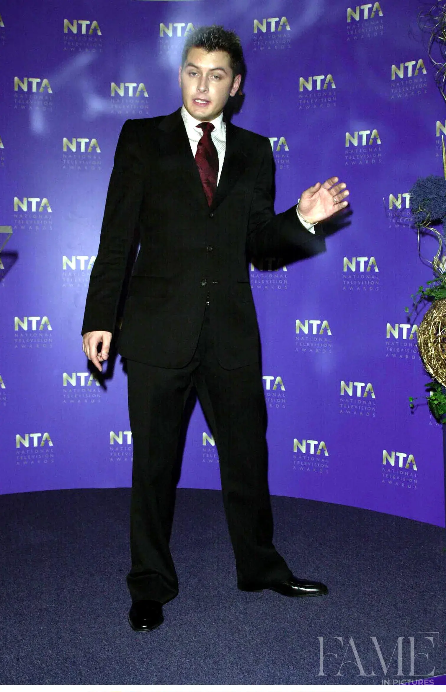 Brian Dowling in a dark suit and tie in front of a purple National Television Awards backdrop