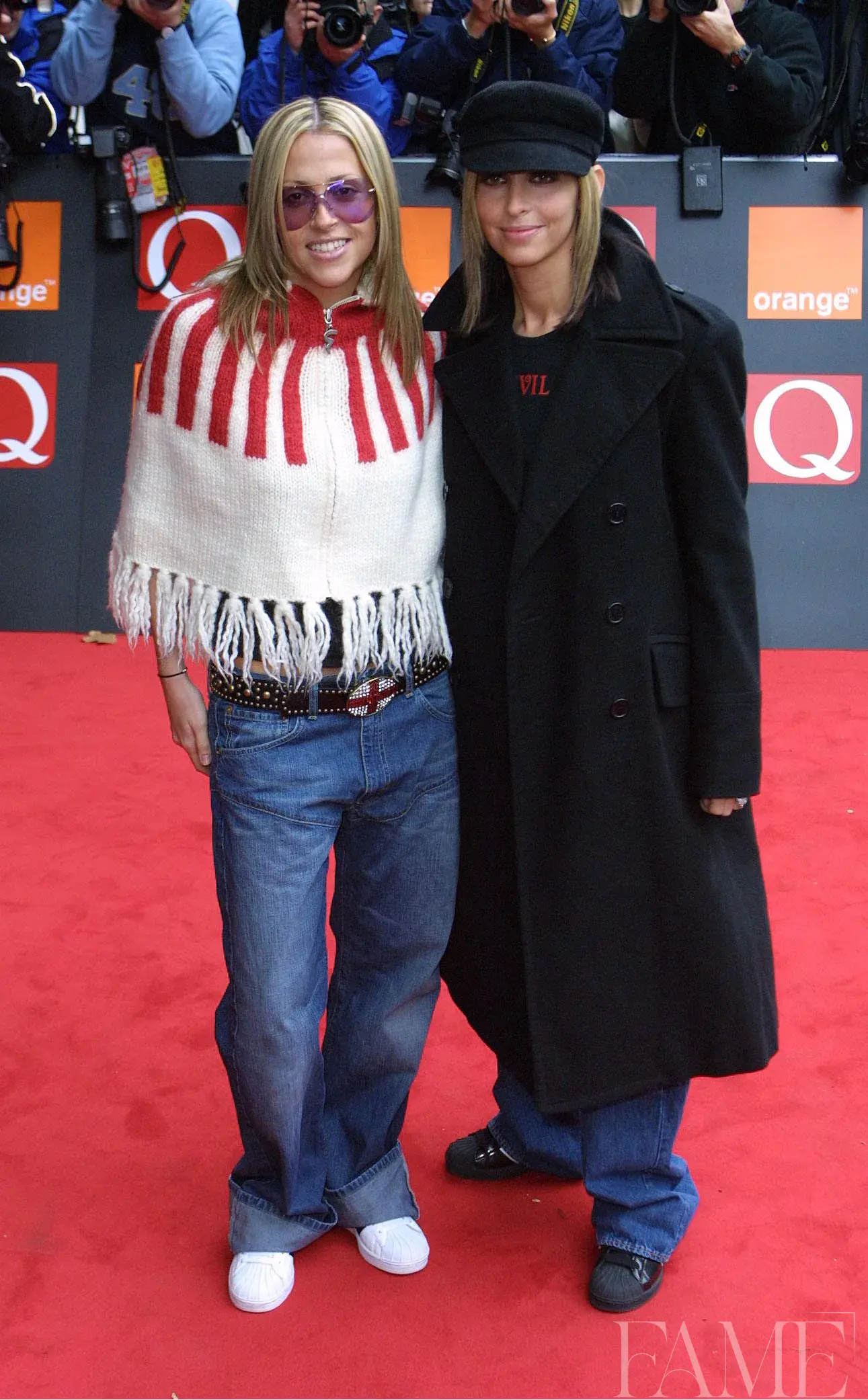 Nicole and Natalie Appleton posing together on the red carpet, wearing a fringed wrap and a long dark coat