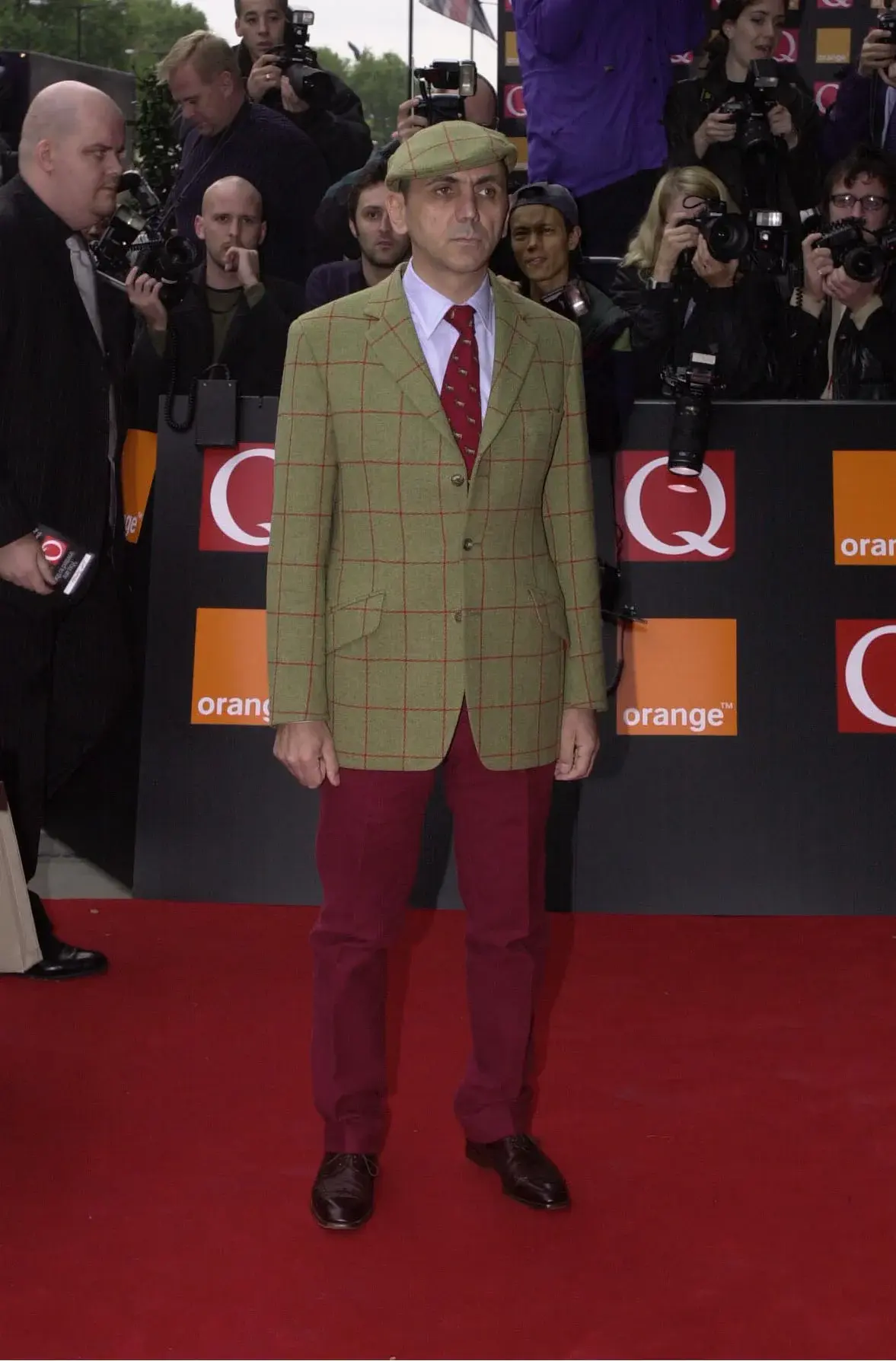 Kevin Rowland in a checked blazer, red tie, red trousers and cap on the Q Awards red carpet