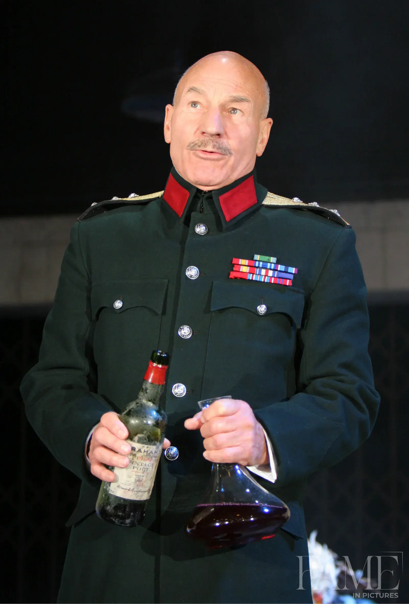 Patrick Stewart as Macbeth in a military-style stage costume, holding a bottle and a glass vessel
